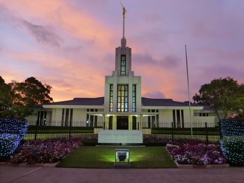 The front entrance to the Sydney Australia Temple, including a partial view of the grounds and fence and a view of the temple name sign.