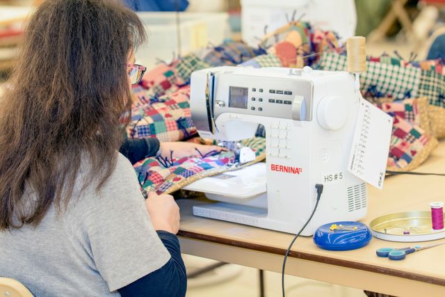 Woman sewing on sewing machine, binding a quilt, at the LDS Humanitarian Center. (horiz)