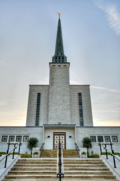 The front steps of the London England Temple leading up toward the temple doors, with the temple’s spire and the angel Moroni statue overhead.