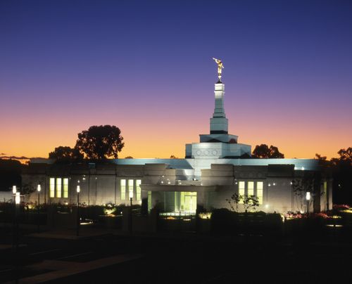 The Adelaide Australia Temple lit up at night in front of a backdrop of a deep purple sky.