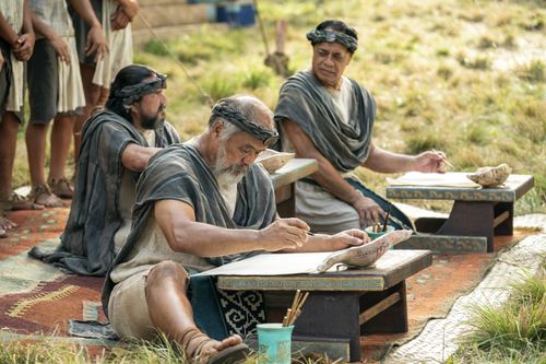 Scribes sit, taking notes on parchment of what King Benjamin is teaching in the Land of Zarahemla.