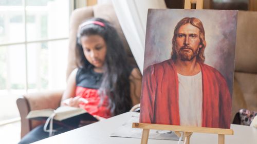 girl sitting next to picture of the Savior