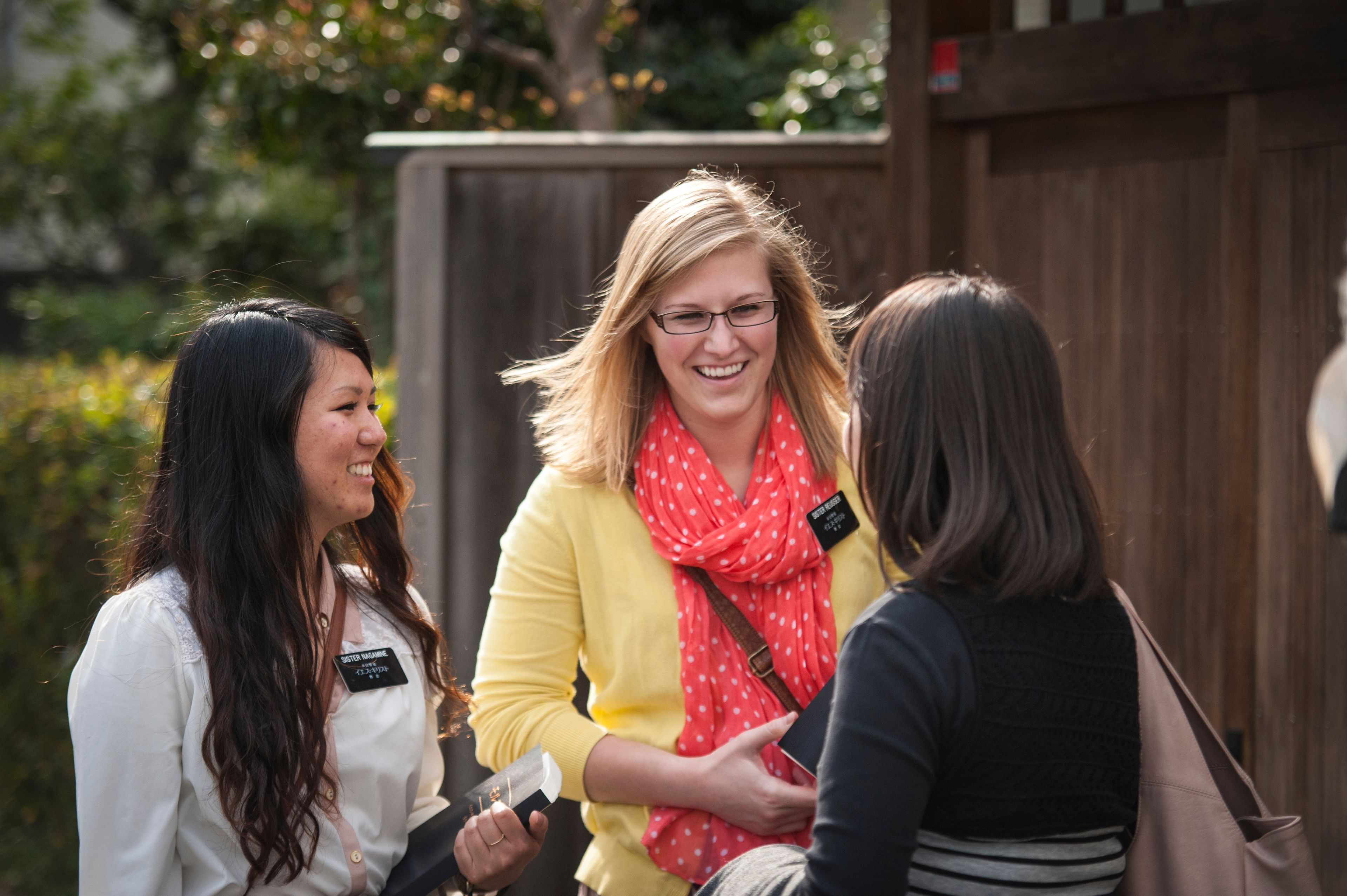 A woman talking to two sister missionaries outside.  