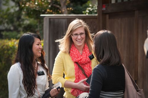A woman in Japan talking to two sister missionaries, one black-haired and one blonde, both holding scriptures.