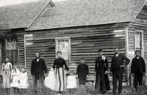 pioneer family in front of log home