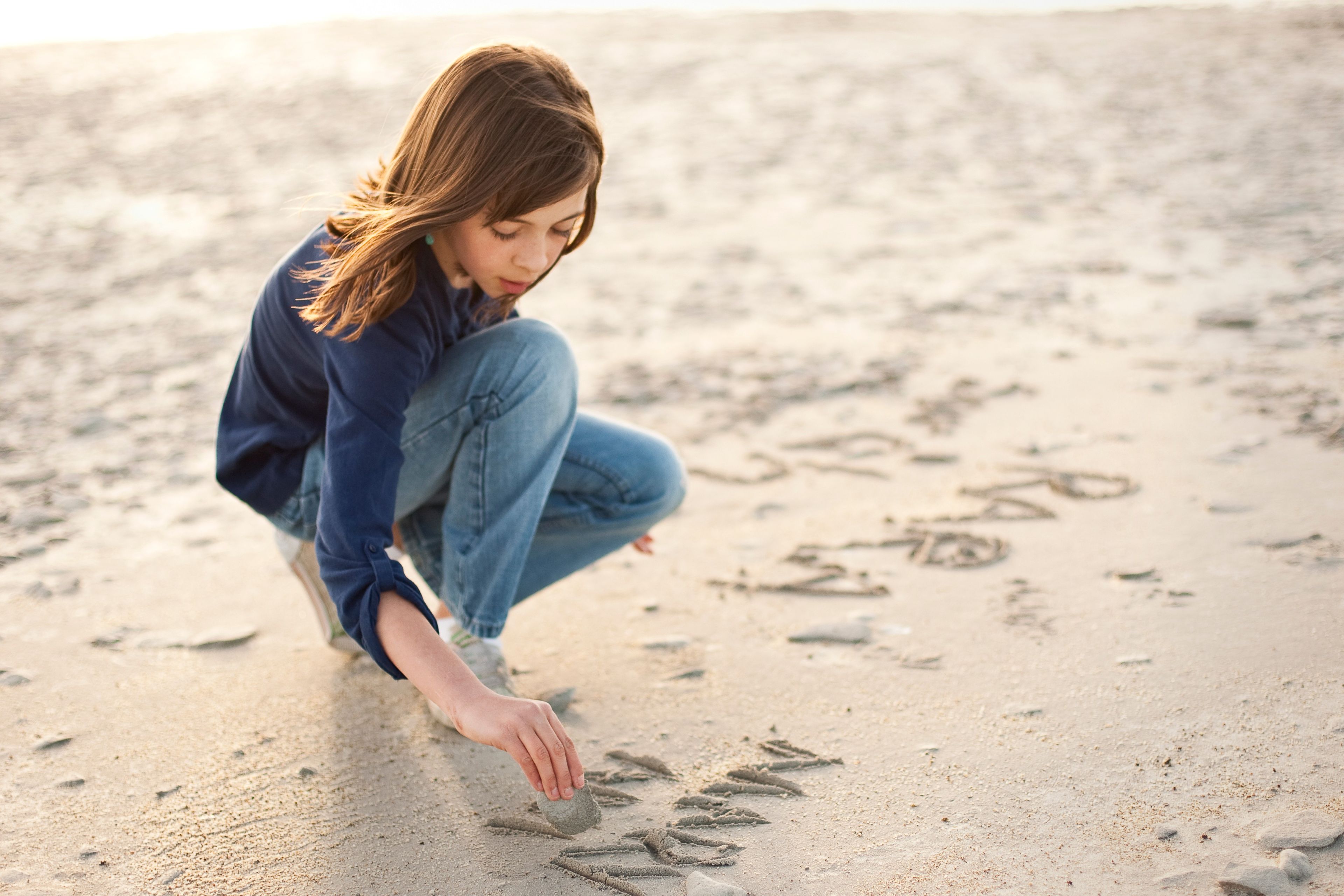 A girl draws in the sand.