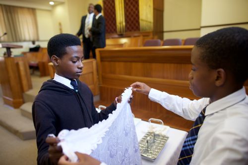 Two young men stand in a  chapel and fold the sacrament cloths.