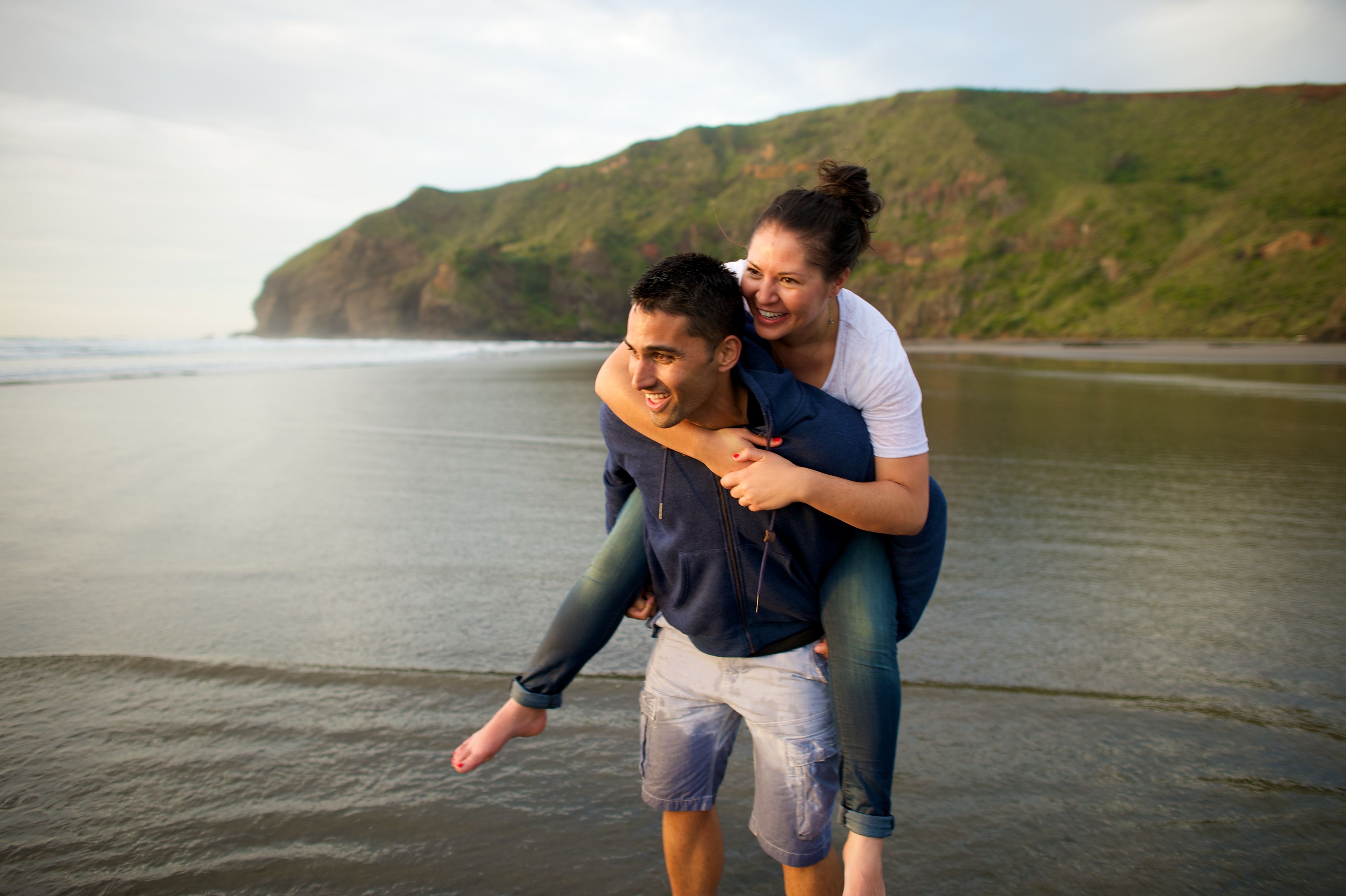 A young man carrying a young woman on his back at a beach in New Zealand.