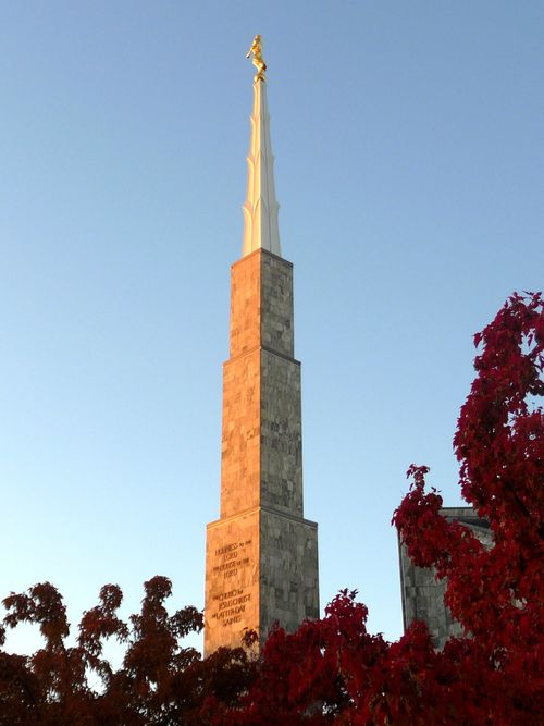 The spire of the Boise Idaho Temple rising above red leaves of fall trees on the temple grounds.