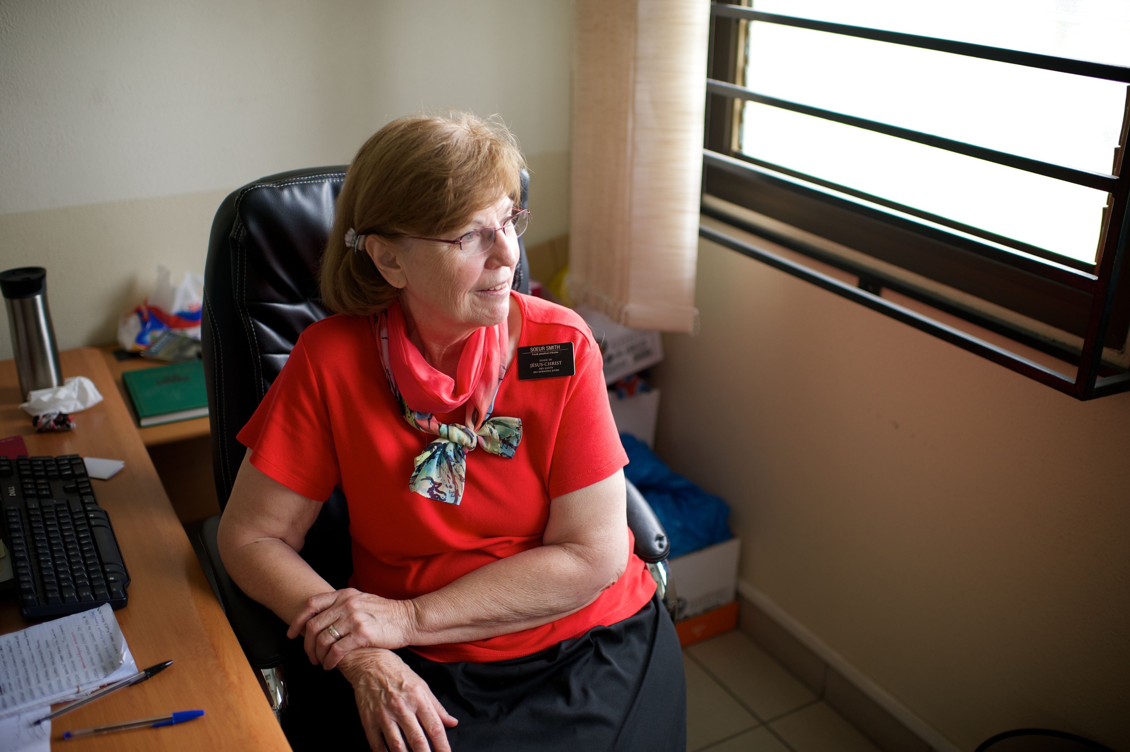 A senior sister missionary sitting at a desk and looking out a window.