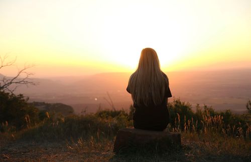 Young adult woman sitting on a mountaintop watching the sunset.