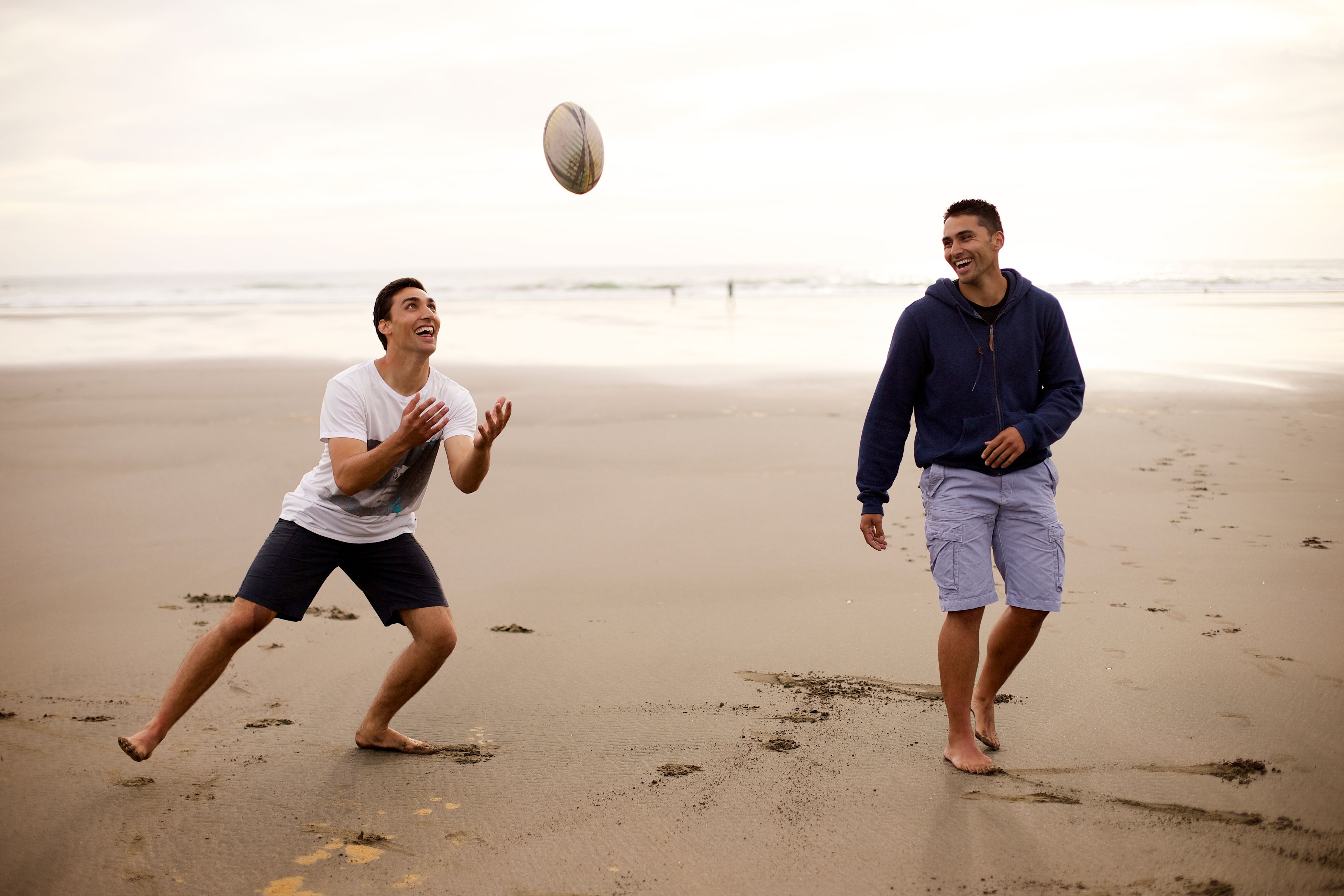 Two young men running on the beach and playing rugby.  