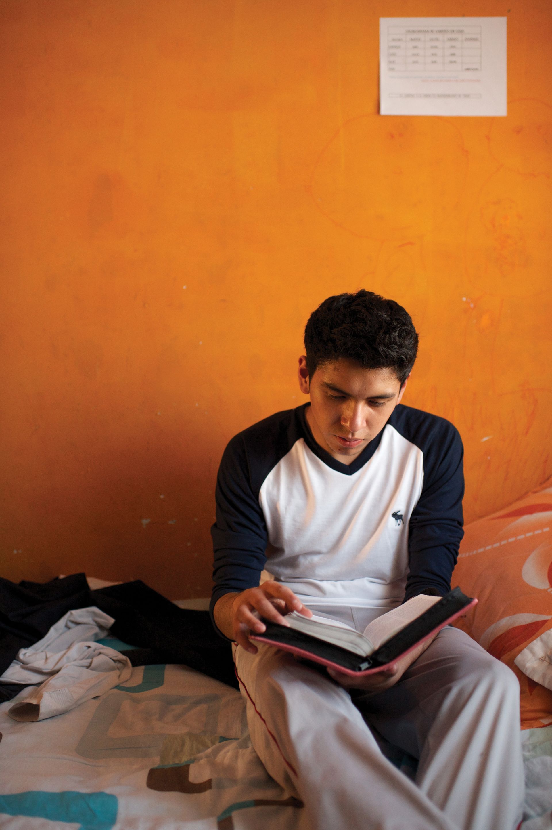 A young man sits on his bed and reads from a set of scriptures.
