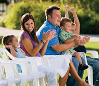 A family sitting together in the Brigham Young Historic Park.  They are sitting on white chairs set up for a concert in the park.