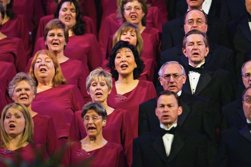 Women in maroon dresses and men in white shirts, black suits, and black bow ties, singing in the Mormon Tabernacle Choir.