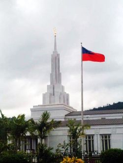 The Samoan flag on the grounds of the Apia Samoa Temple, with the temple’s spire and the angel Moroni seen in the background.