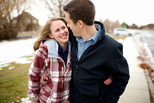 A young man and woman in coats, smiling and embracing each other while walking outside in the winter.
