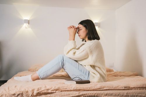 Eine junge Frau sitzt auf dem Bett und betet