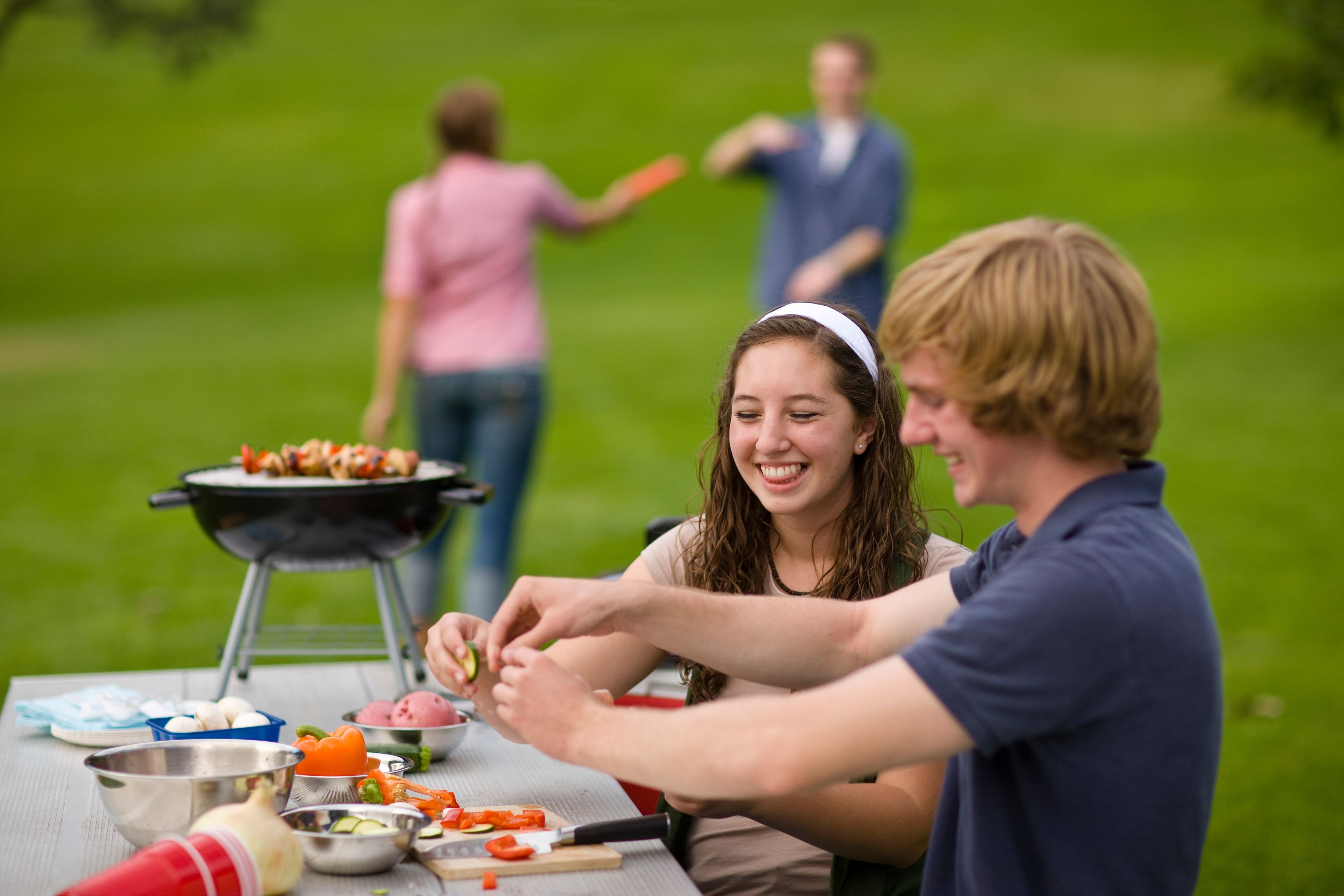 A teenage couple preparing food on a table at the park.  