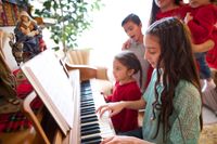 Young girl plays the piano as her family watches.