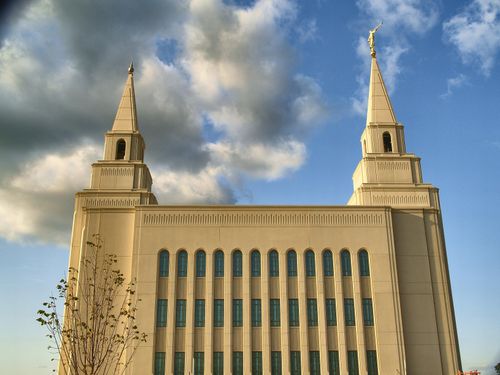 A side view of the Kansas City Missouri Temple, with a small tree in the foreground and a large cloud on the left side.