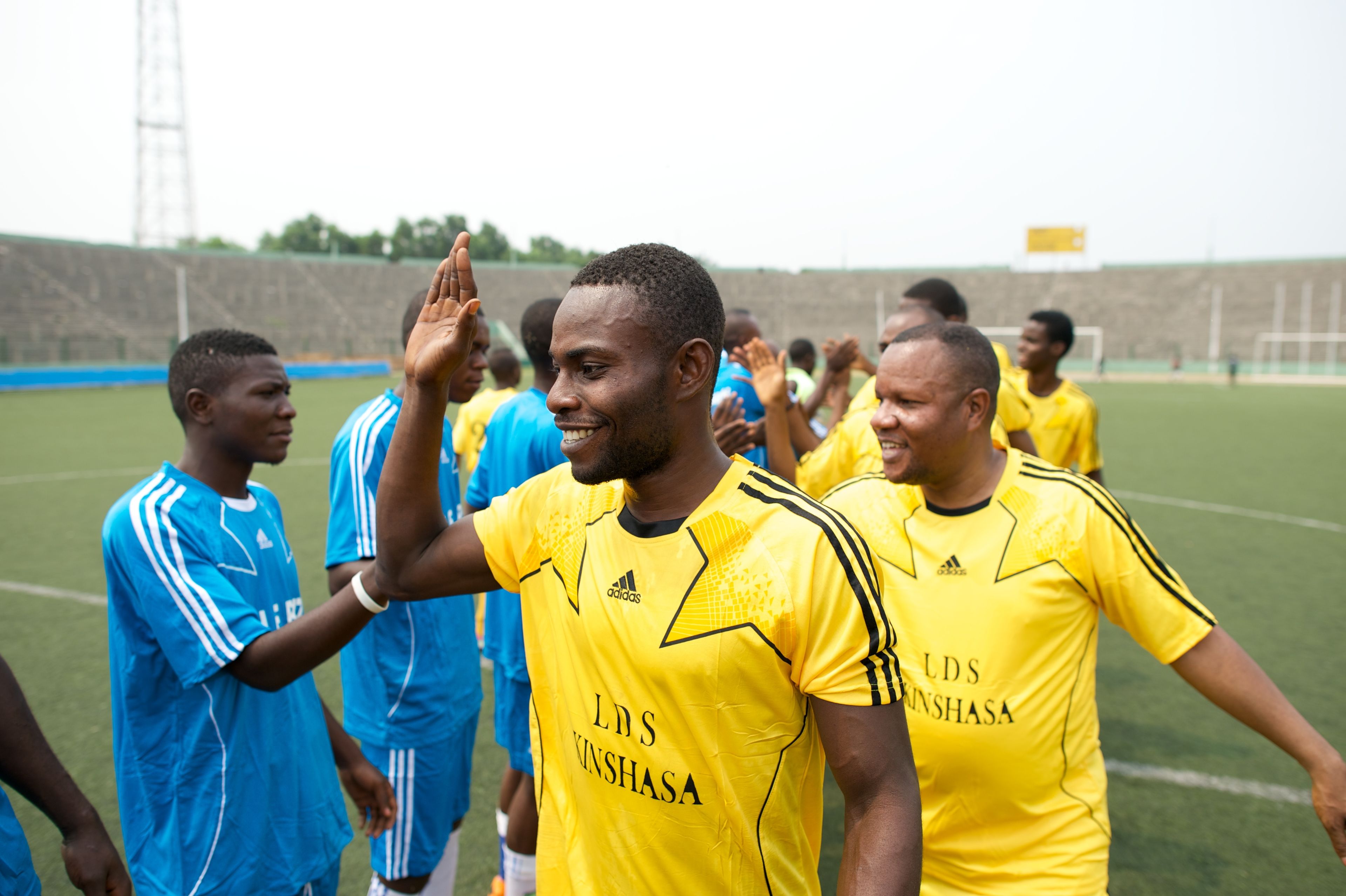 Men from Africa walk in two lines, giving high fives to the opposite team at a soccer game.  