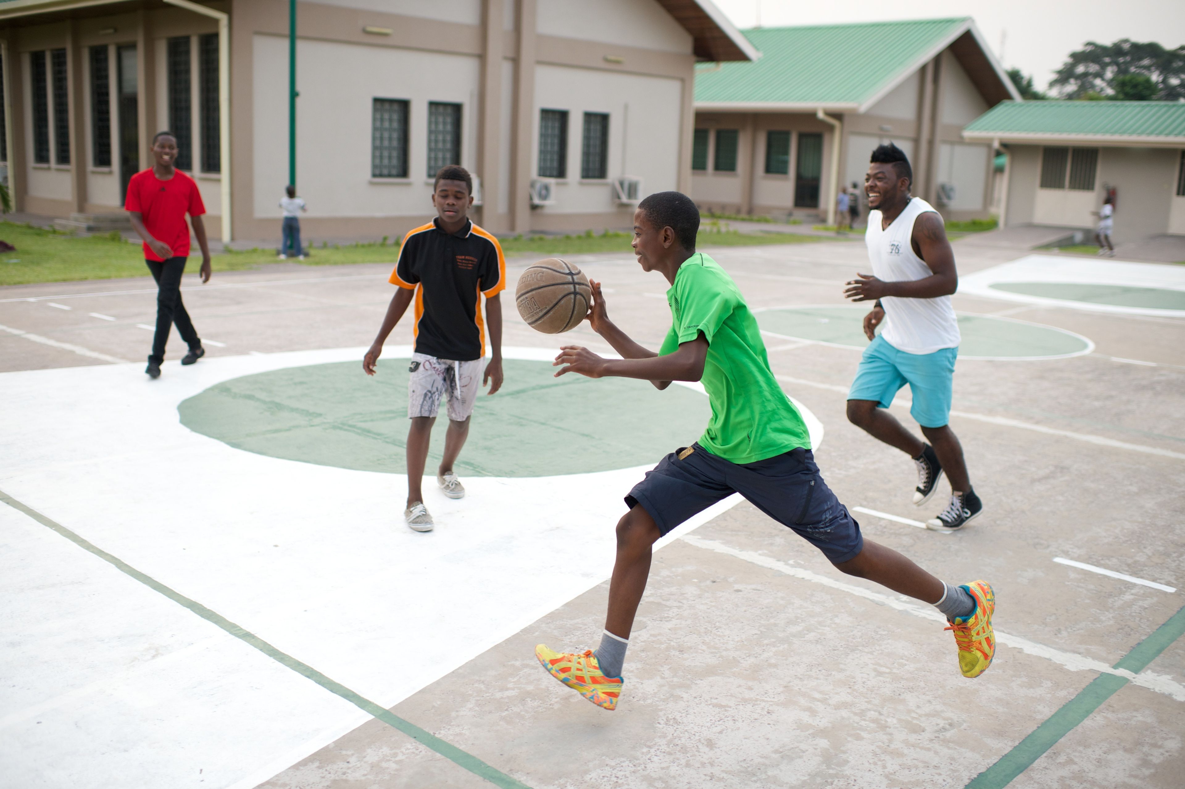 A young man from Africa quickly runs and dribbles a basketball with other players nearby.