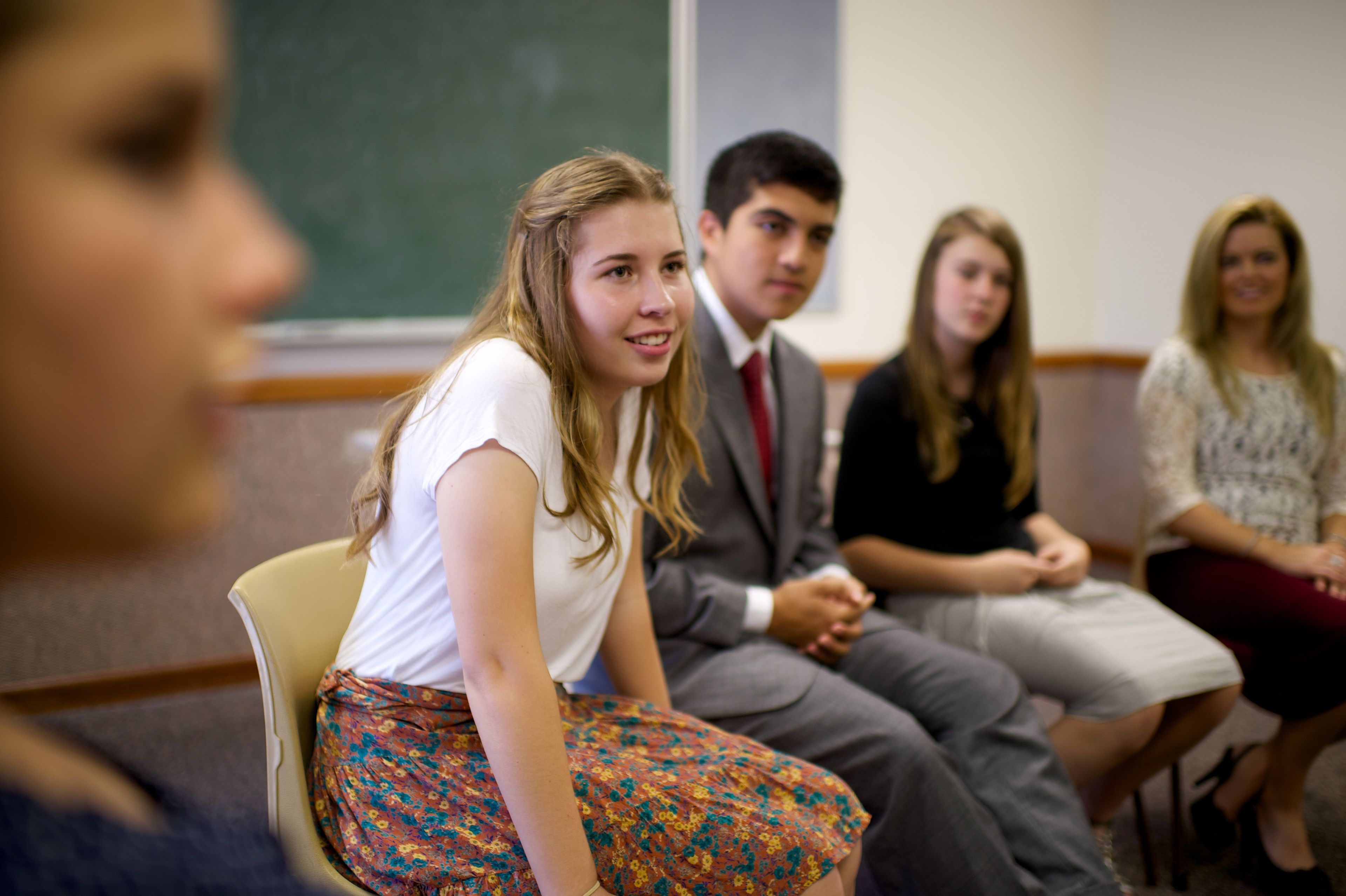 A young woman sits in Sunday School surrounded by other young men and young women.