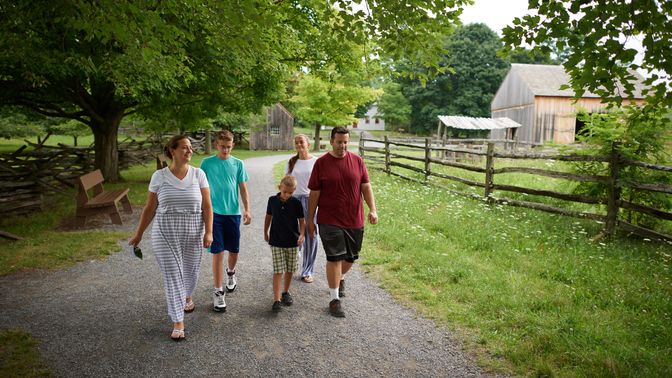 Various people walk the paths around the Sacred Grove. There are lots of trees around and everything is very green. The families are all walking on dirt pathways.