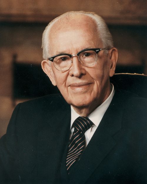 A portrait photograph by Busath Photography of Ezra Taft Benson in a dark suit and striped tie, sitting in a chair.