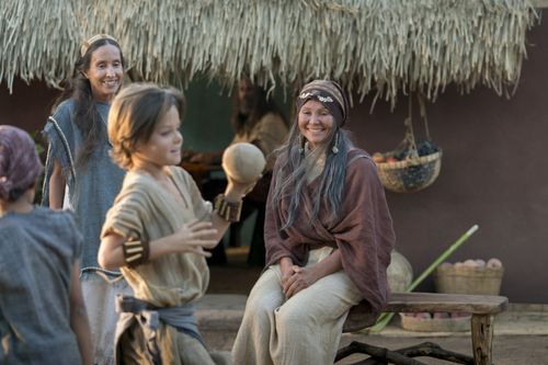 Nephi’s wife sits outside with the children as they play.