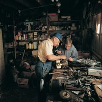 A father and teenaged son are working together on a small motor in a home workshop