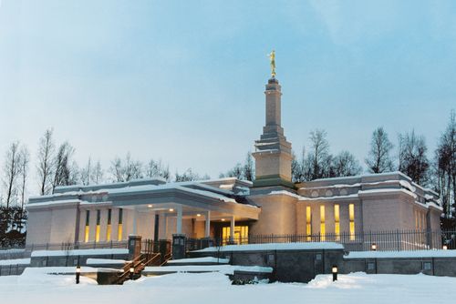 A view of the front of the Anchorage Alaska Temple on a snowy evening, with the lights glowing inside the windows.