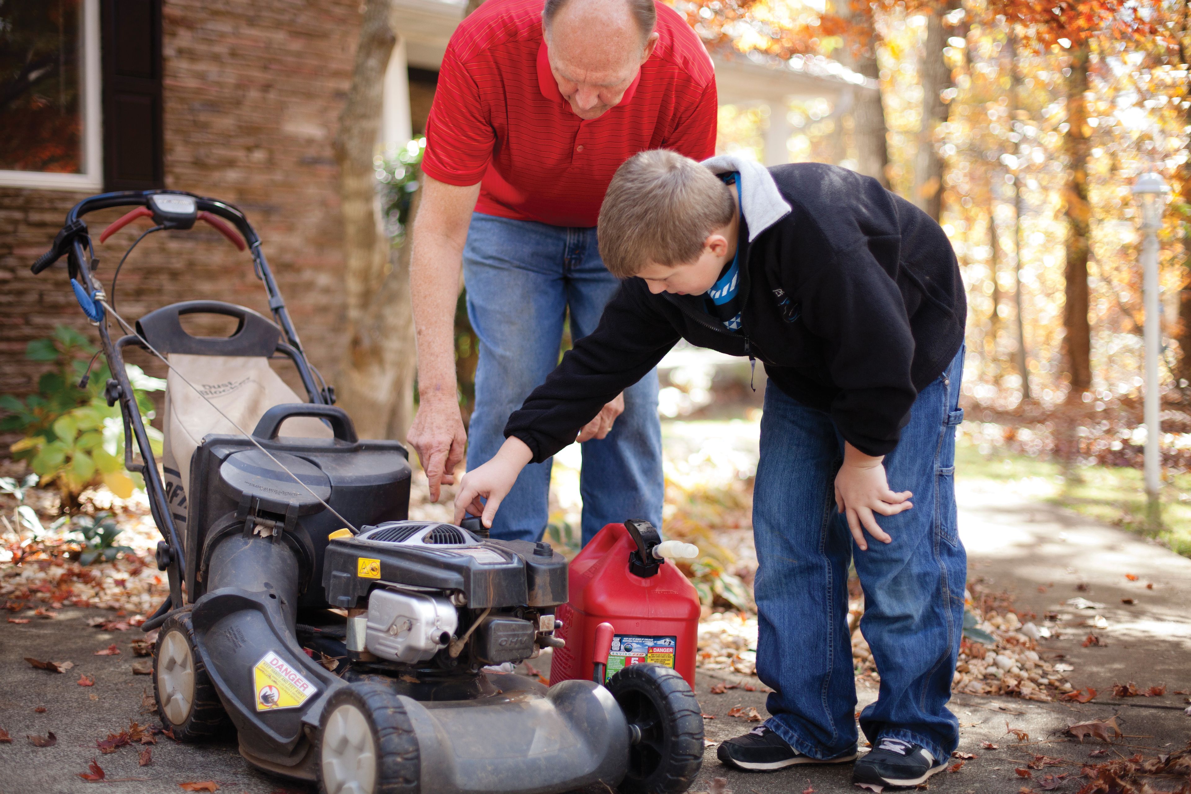 A father teaches his son how to use a lawn mower.