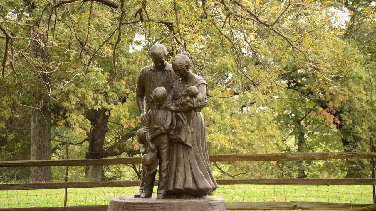 Bronze statue depictions of a man, boy, and woman holding a baby and standing together with their heads bowed.