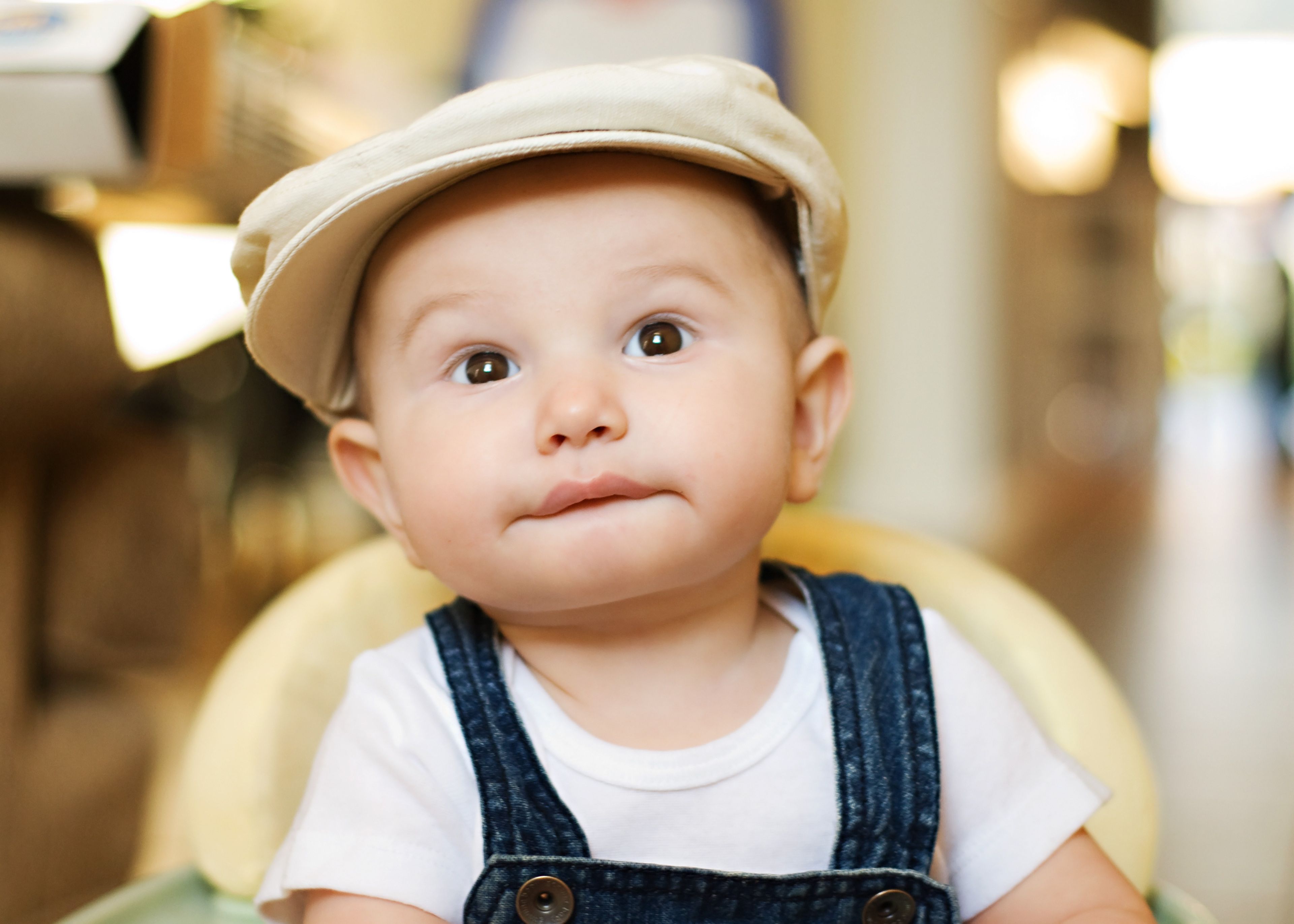 A baby boy in overalls and a hat.