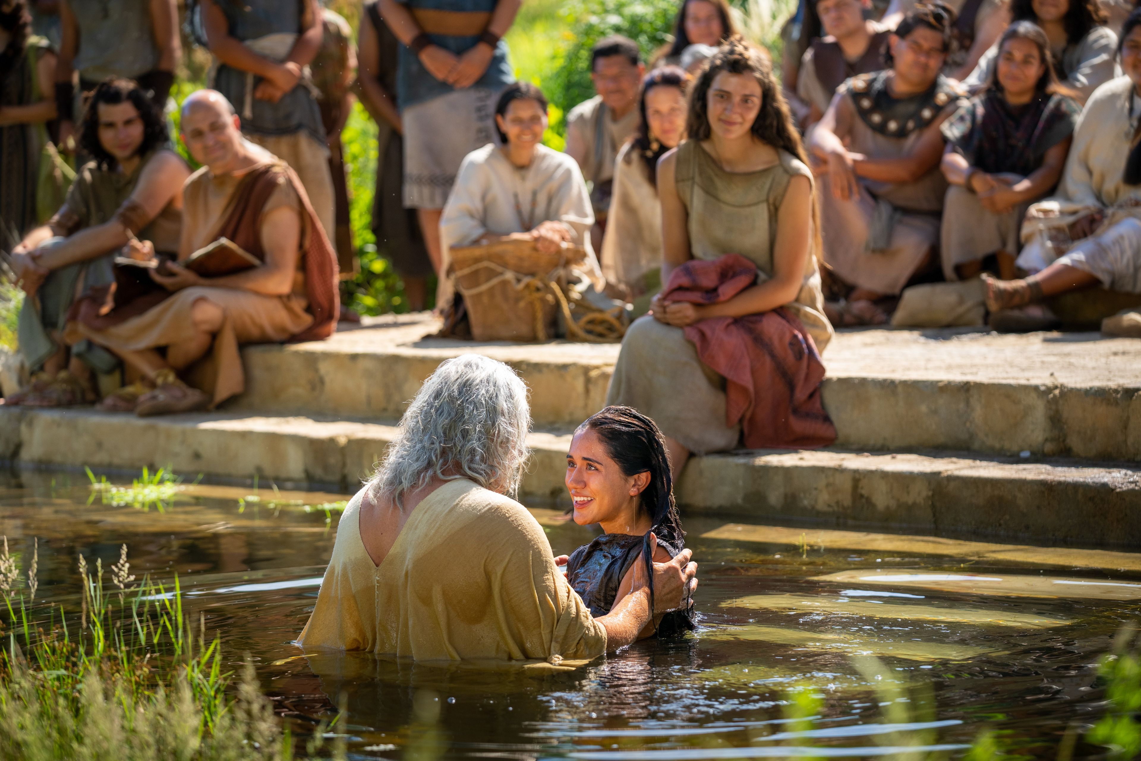 Nephi, son of Nephi, baptizes other Nephites in a river. Others (including Timothy and Jonas) stand at the water's edge and watch.