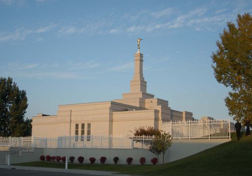 The Bismarck North Dakota Temple exterior in the light of the late afternoon, with two people walking on the grounds in the distance.