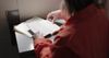 An inmate is insider her cell. She sits at a table and studies the scriptures.