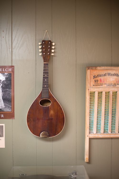 A mandolin hangs on a gray wall next to an old washboard and poster.