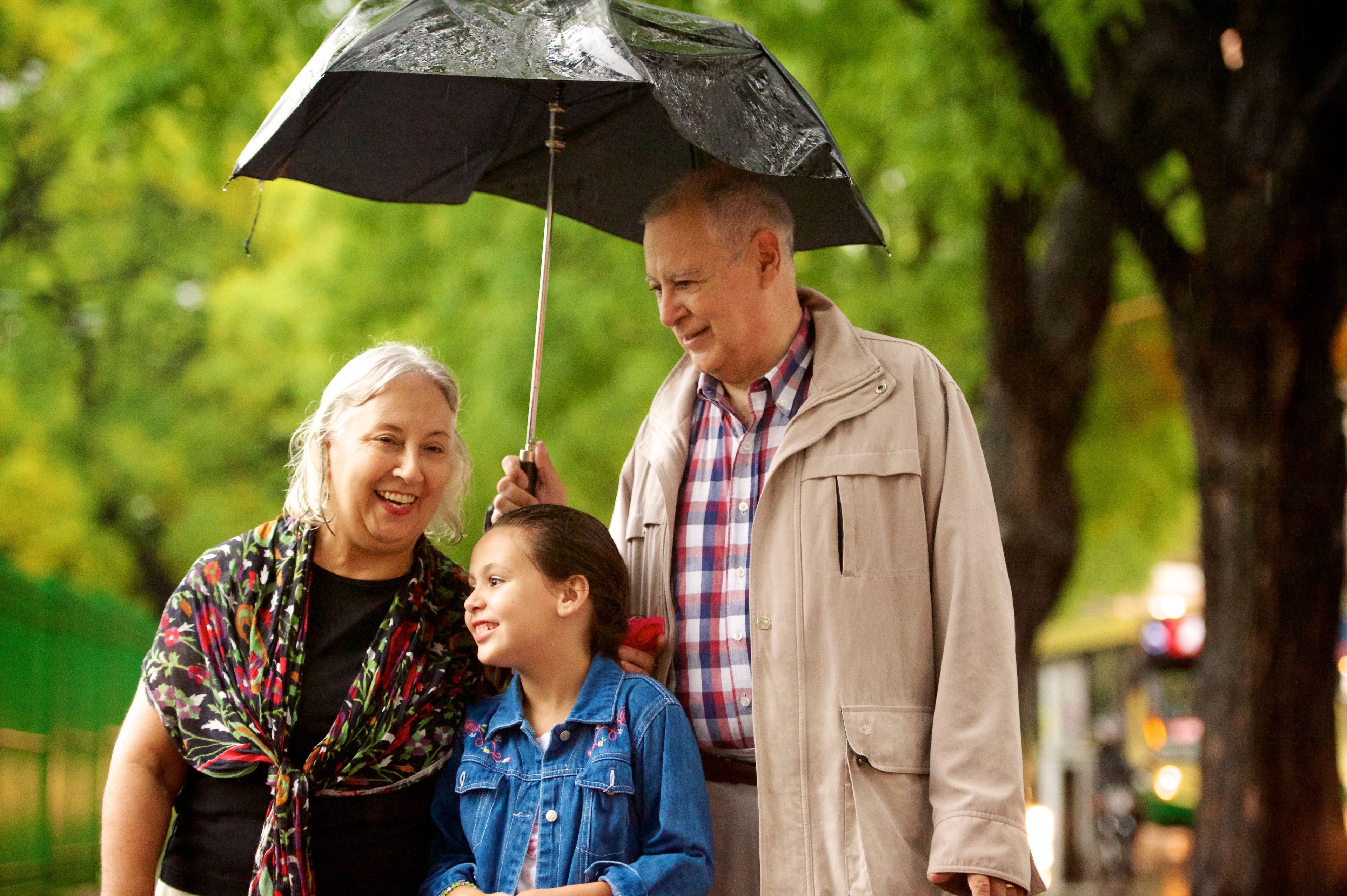 Grandparents walk with their granddaughter under an umbrella.