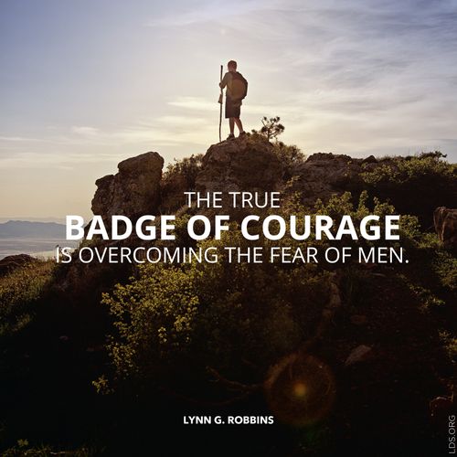 A photograph of a Scout standing on a mountain, with a quote by Elder Lynn G. Robbins: “The true badge of courage is overcoming the fear of men.”