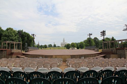 Rows of empty chairs and an empty stage at the Nauvoo Pageant, with the city of Nauvoo as a backdrop.