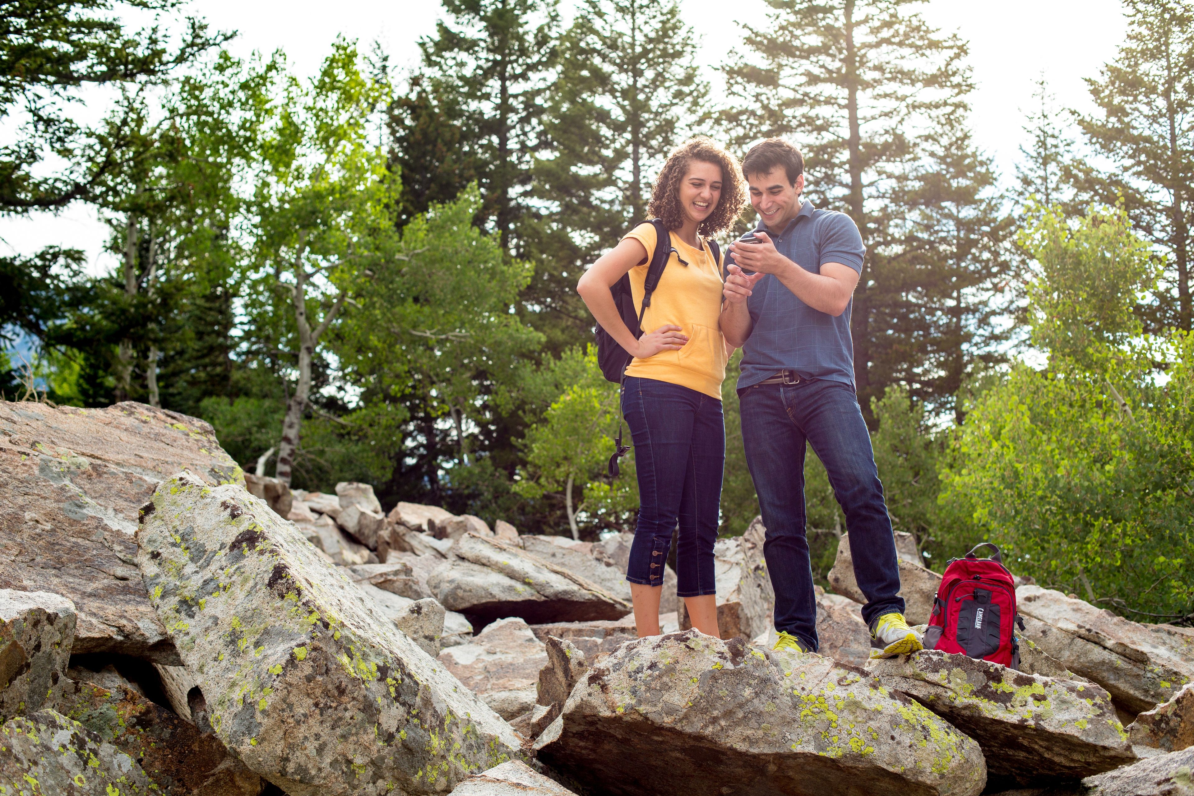 A man and woman look at a phone while hiking.