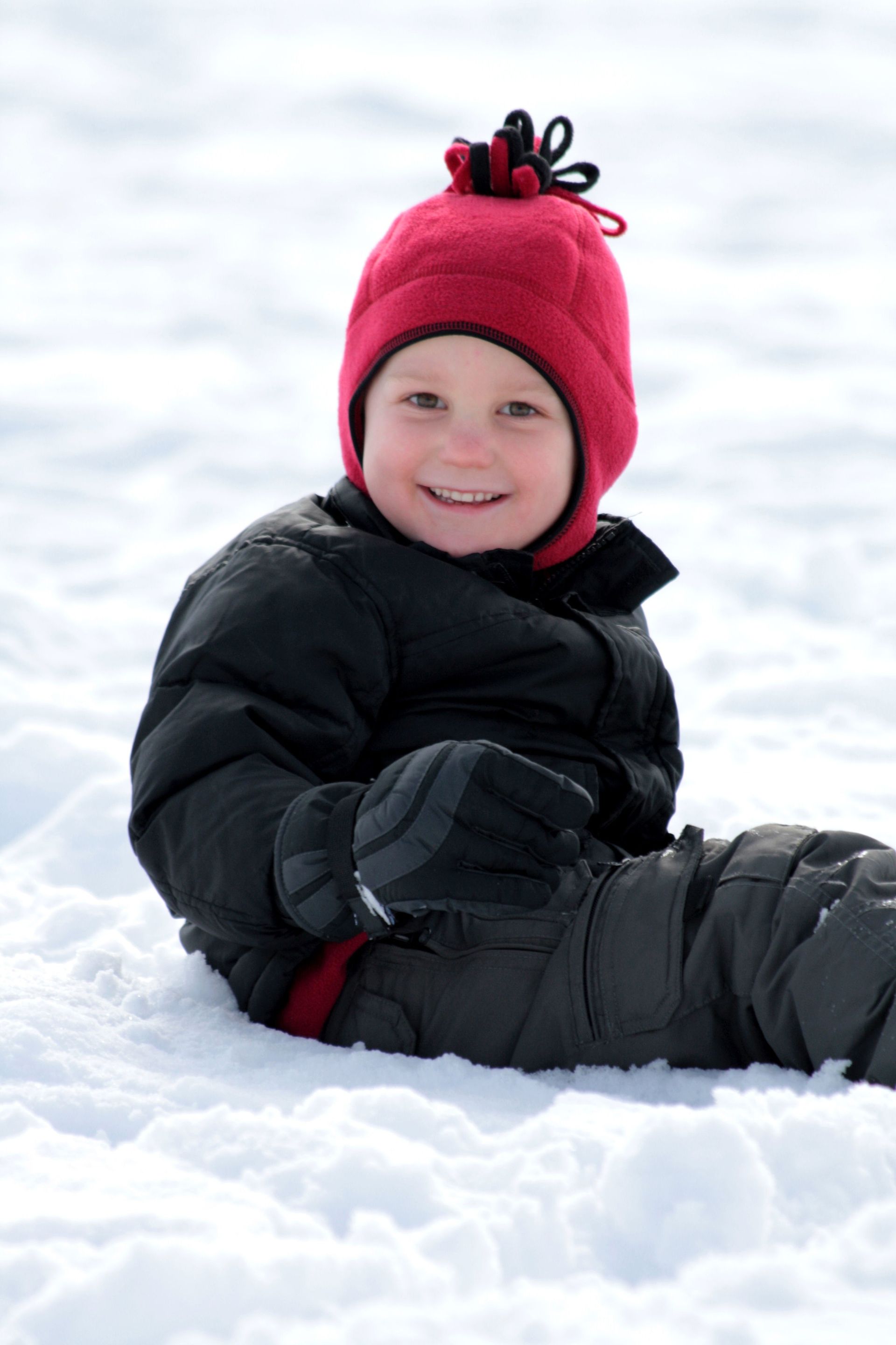 A little boy in a red hat plays in the snow.