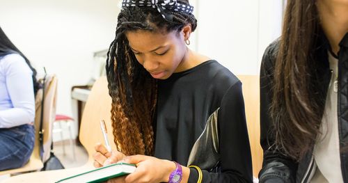 A group of young women are shown looking at a teacher. They discuss and talk together with each other.