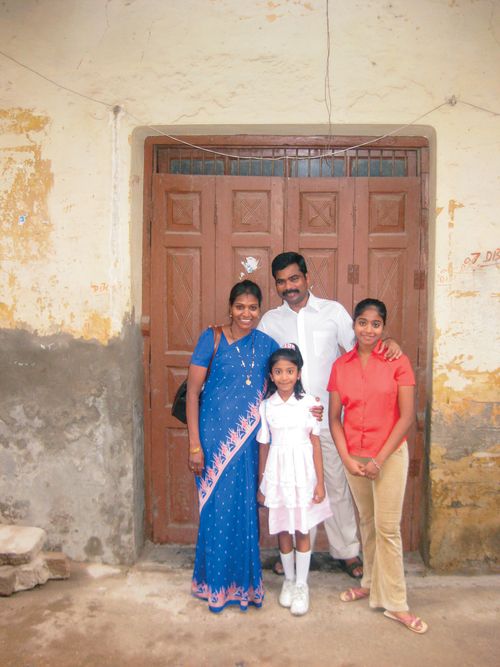 A mother and father stand in front of a door with their two children.
