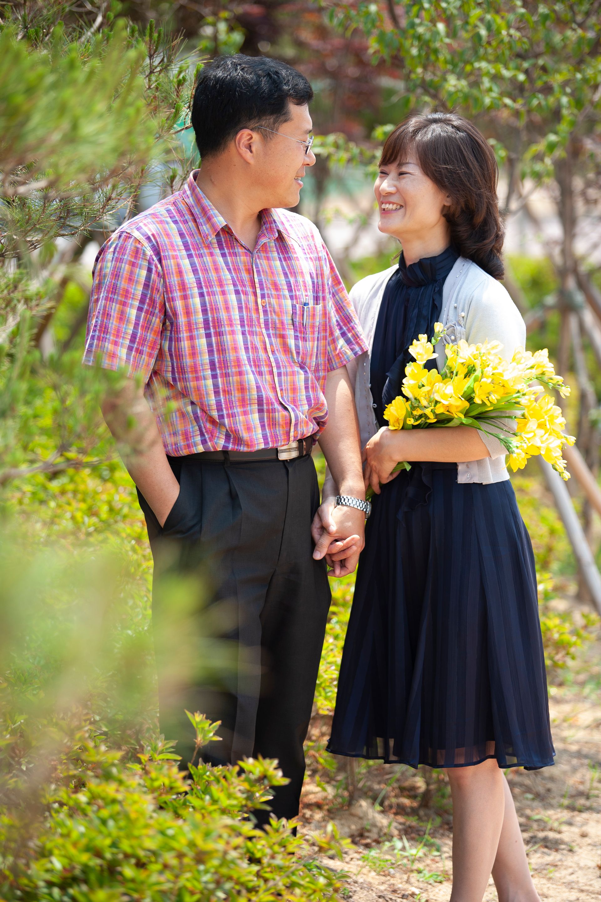 A Korean couple standing and smiling at each other.