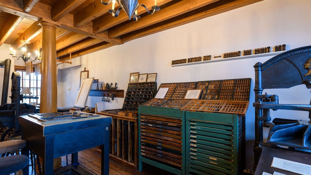 Interior view of a print shop shows a compositor’s table with boxes of type. 