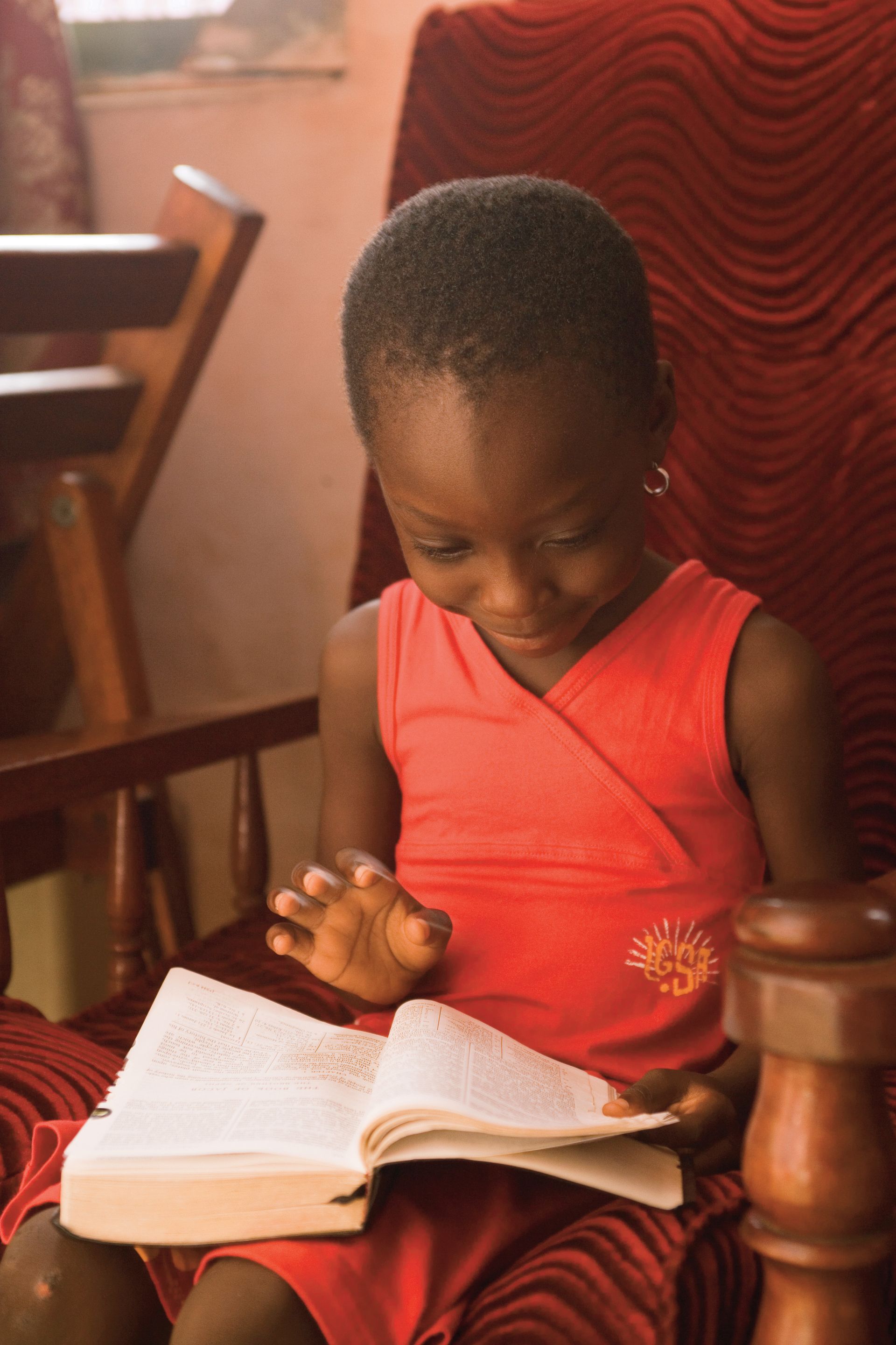 A little girl sits in a chair and flips the pages of a set of scriptures.